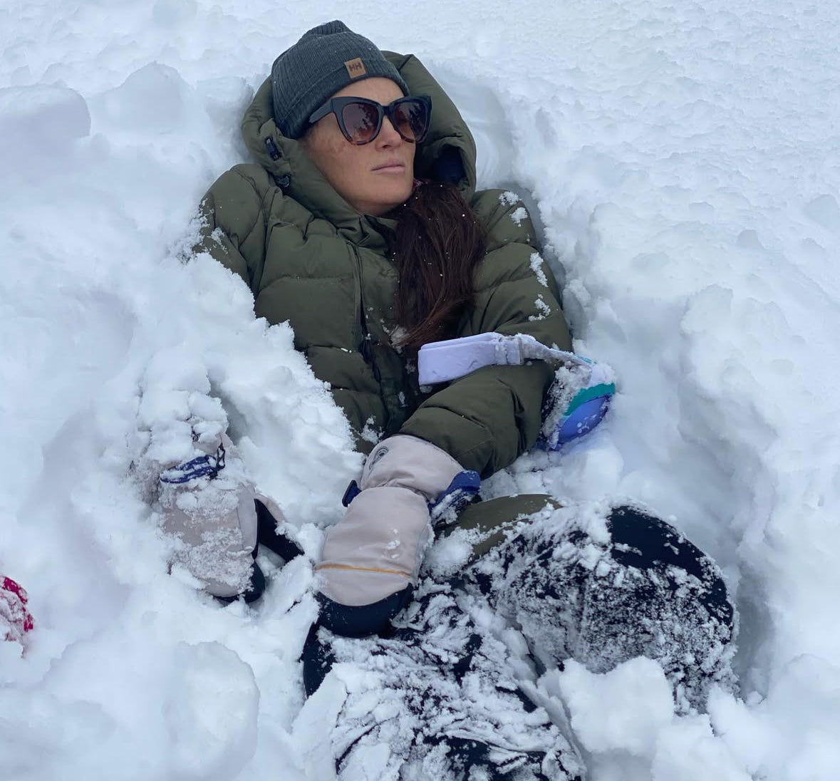 Person lying in the snow wearing winter clothing and sunglasses