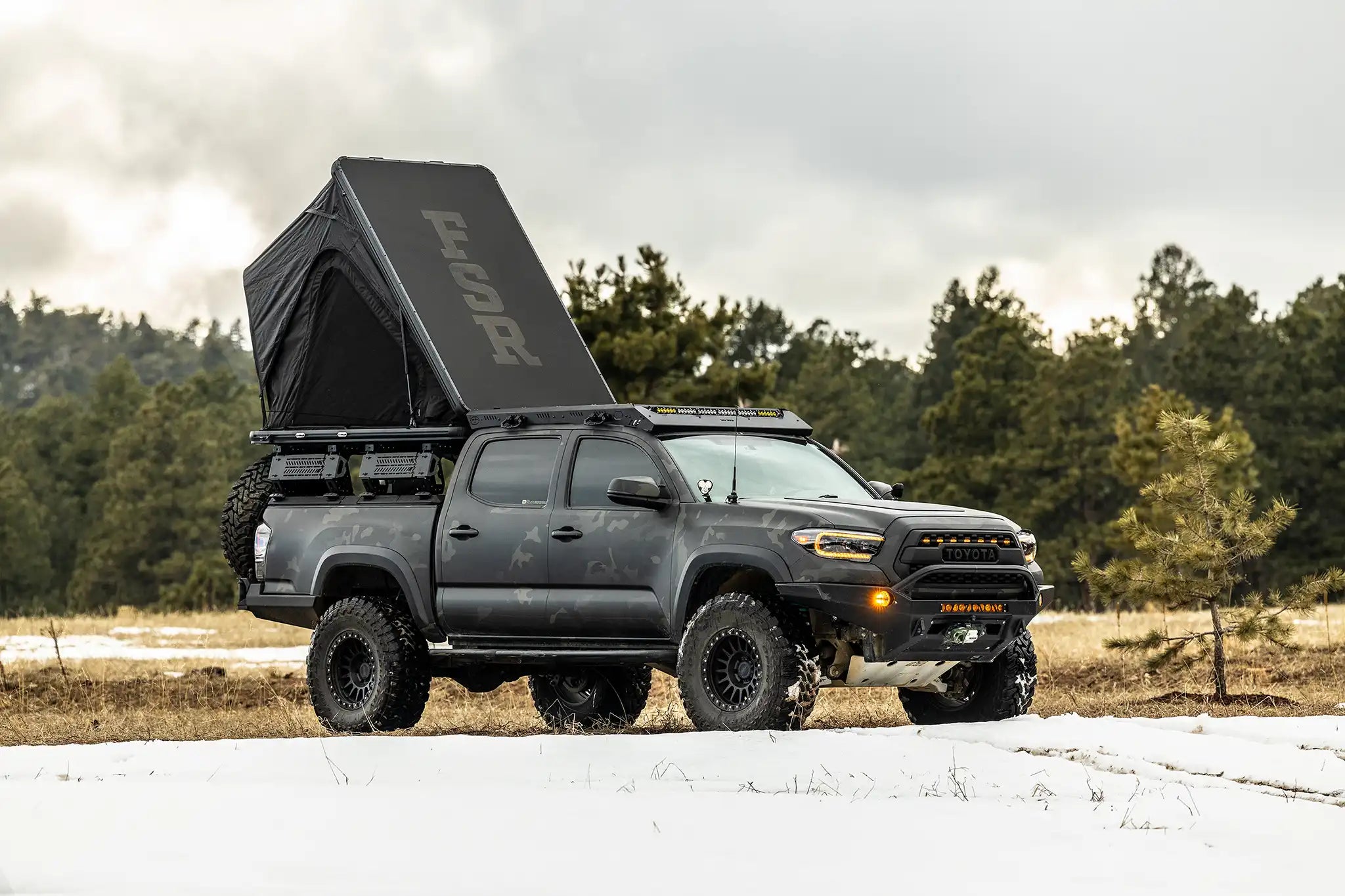 Black pickup truck with a rooftop tent in a forested area