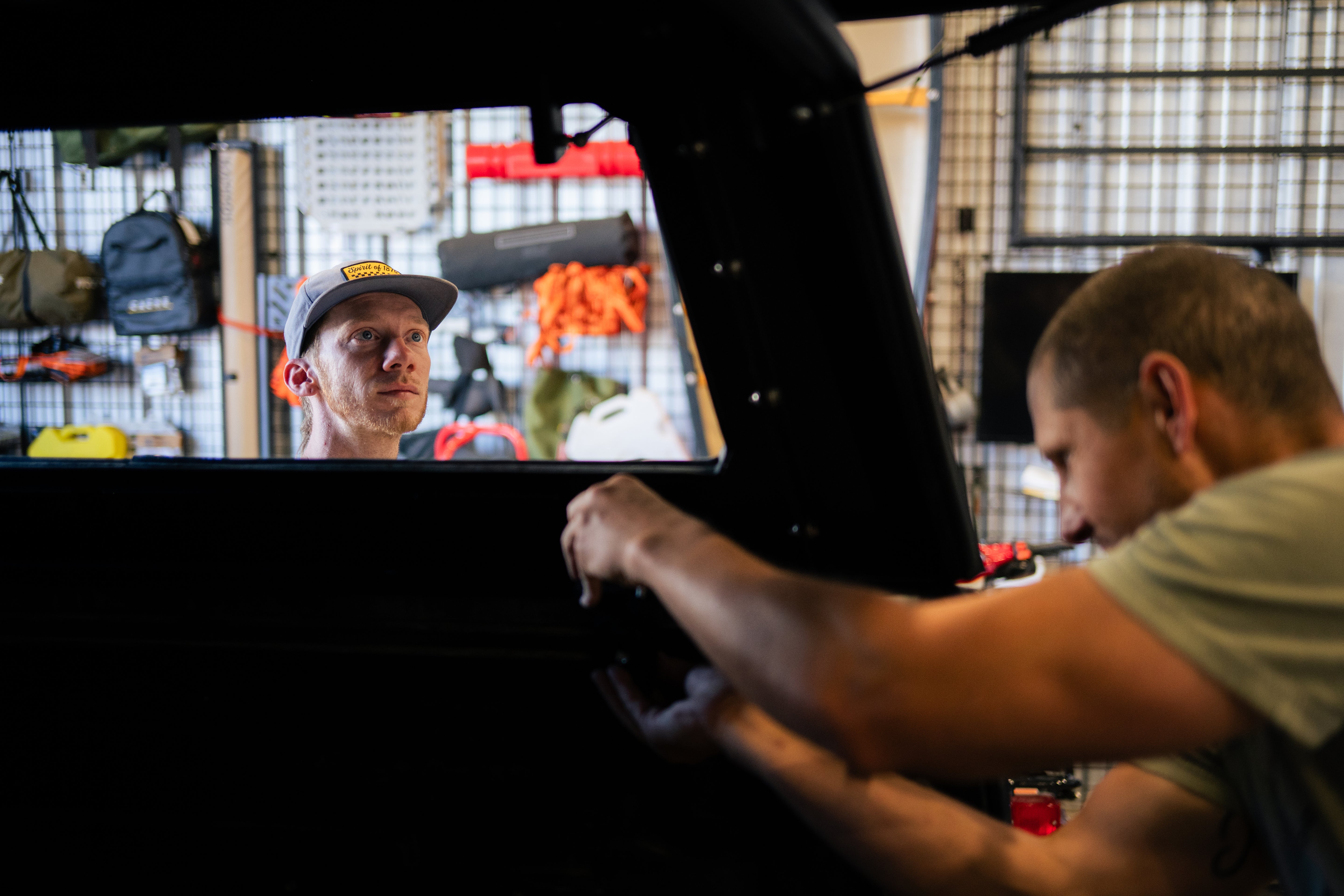 Two men working on a vehicle interior in a workshop setting.