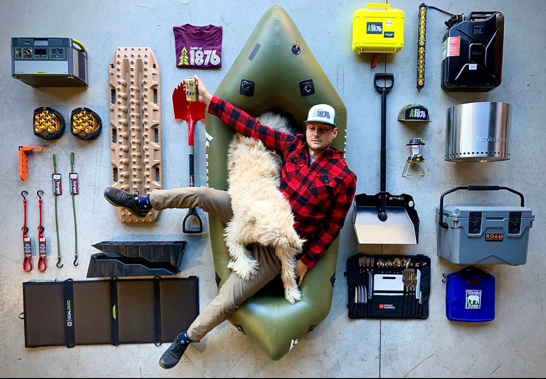 Person sitting in a green inflatable kayak surrounded by outdoor gear on a gray floor.