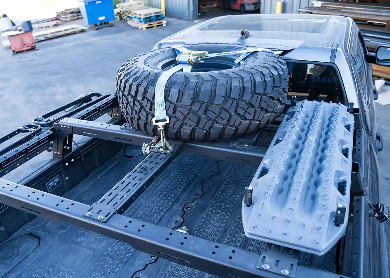 Truck bed with tire and snow shovels, parked in a lot.