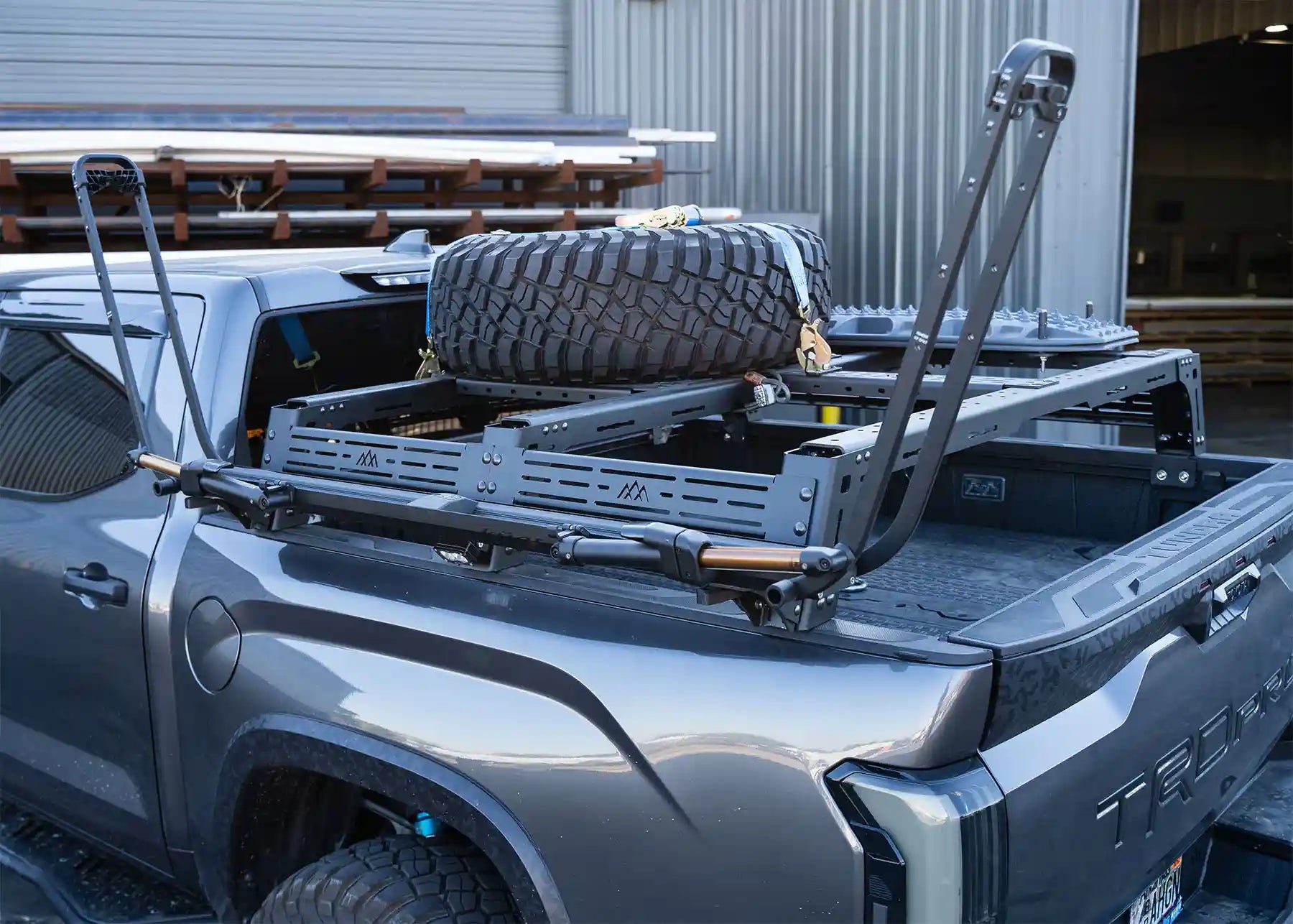 Truck bed with storage rack and tire, parked in a warehouse setting