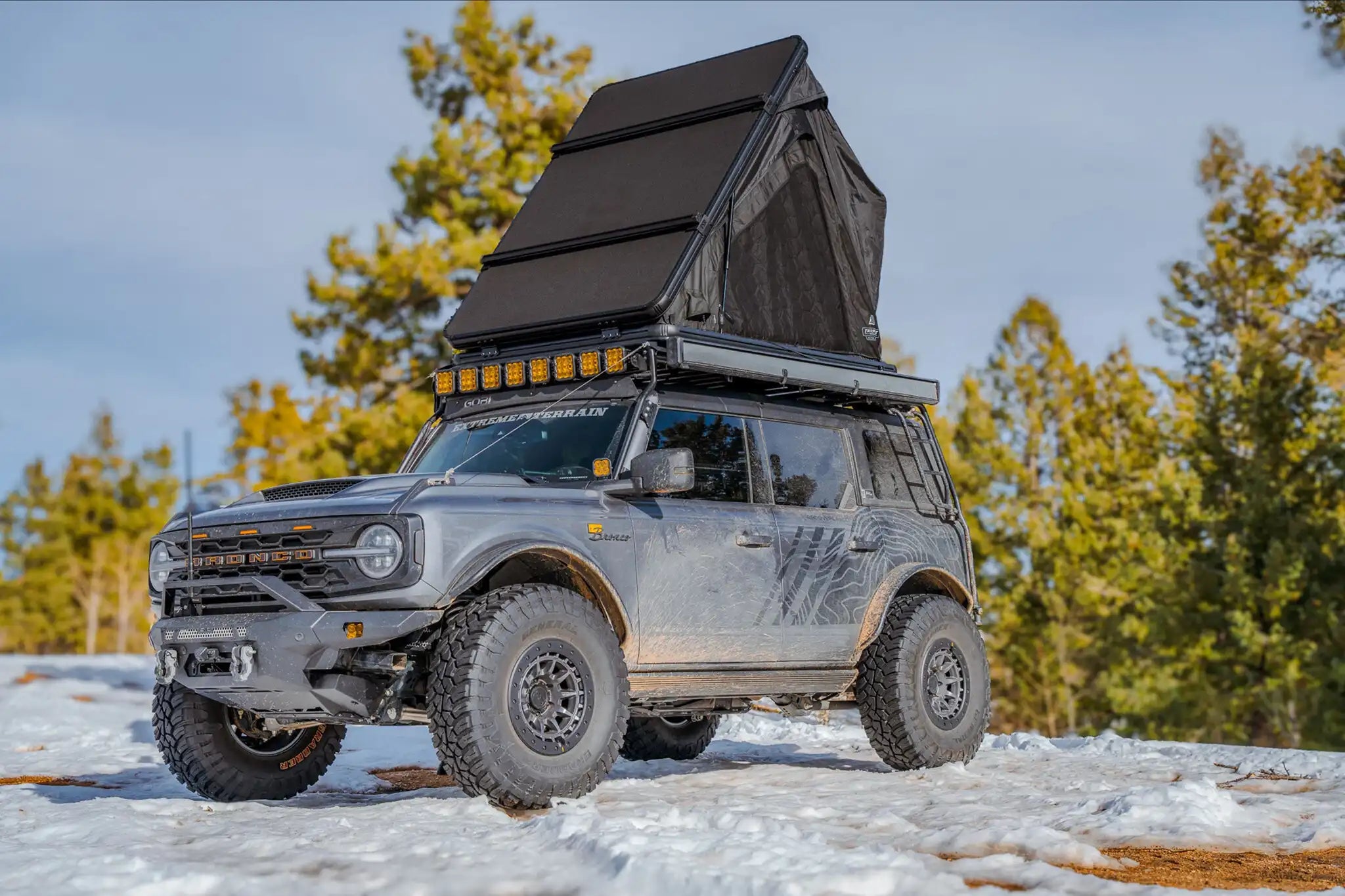 SUV with a rooftop tent parked on a snowy landscape with trees in the background