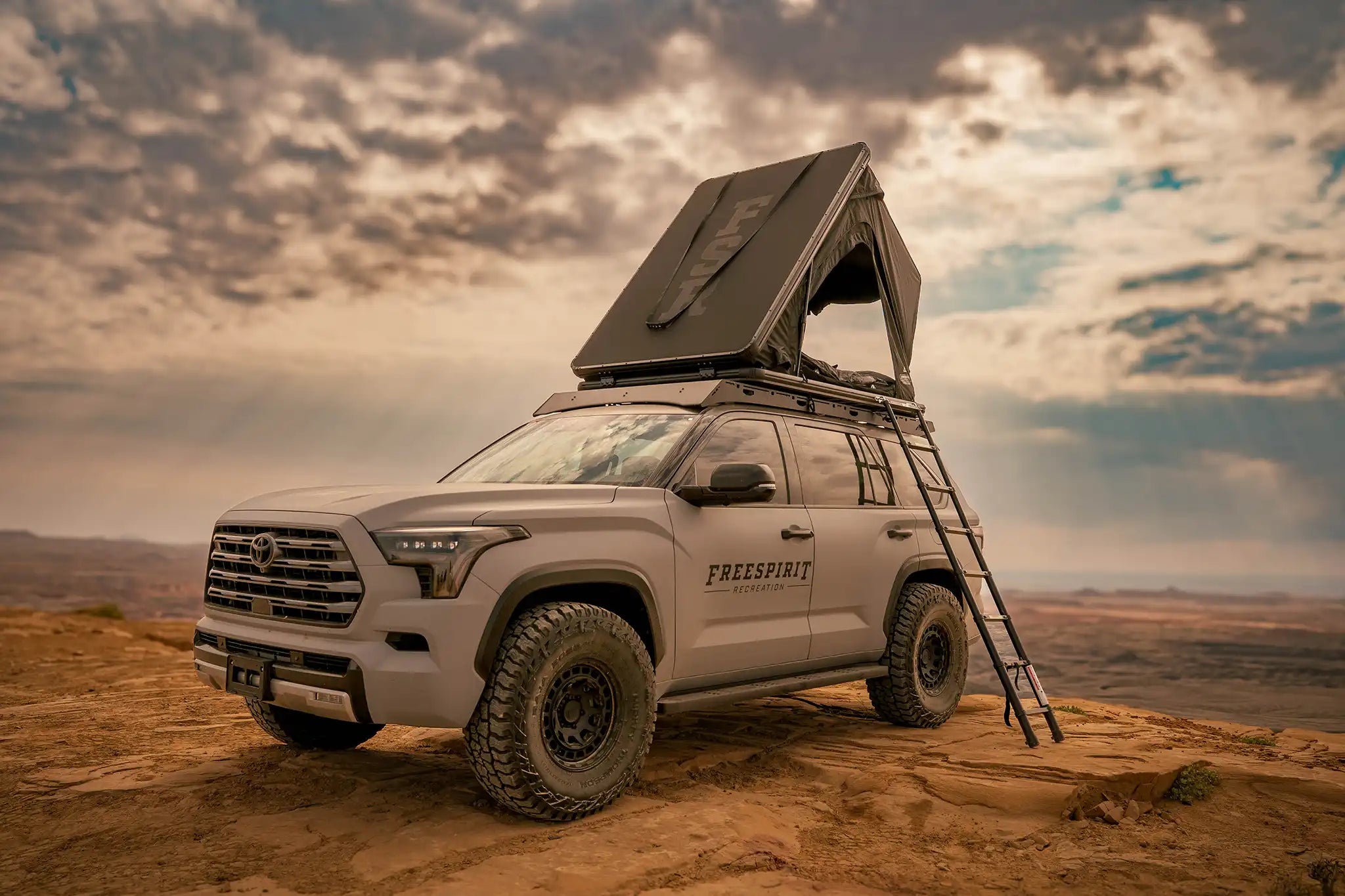 Silver SUV with a roof tent on a desert landscape