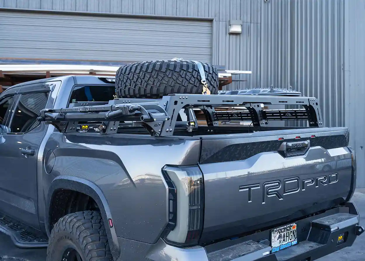 Gray Toyota Tundra truck with roof rack and spare tire, parked in front of a building.