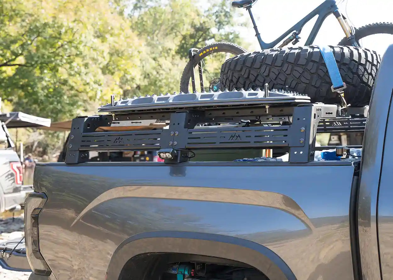 Truck bed with a bike rack and a bicycle loaded on top, set against a natural background.