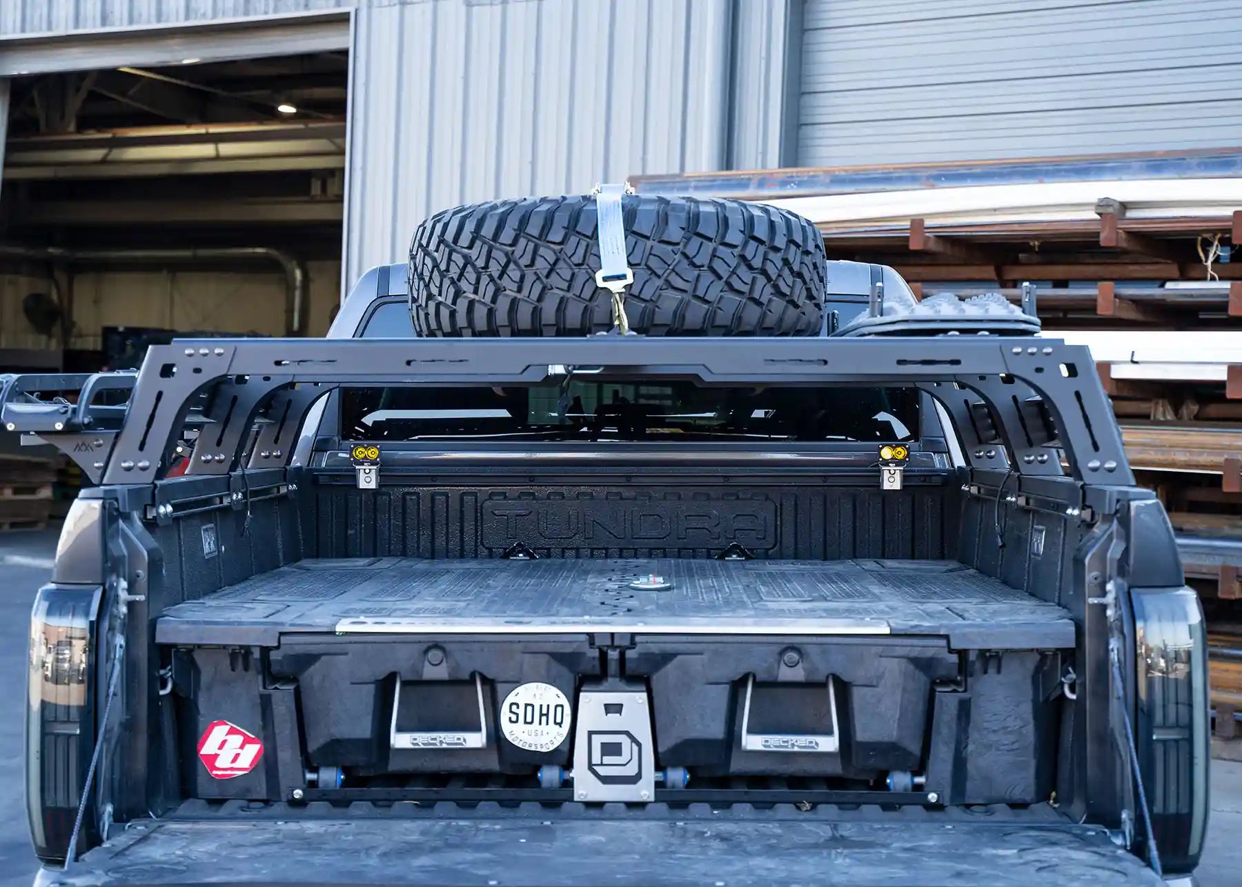 Back of a truck with a spare tire mounted on the tailgate, parked inside a warehouse.